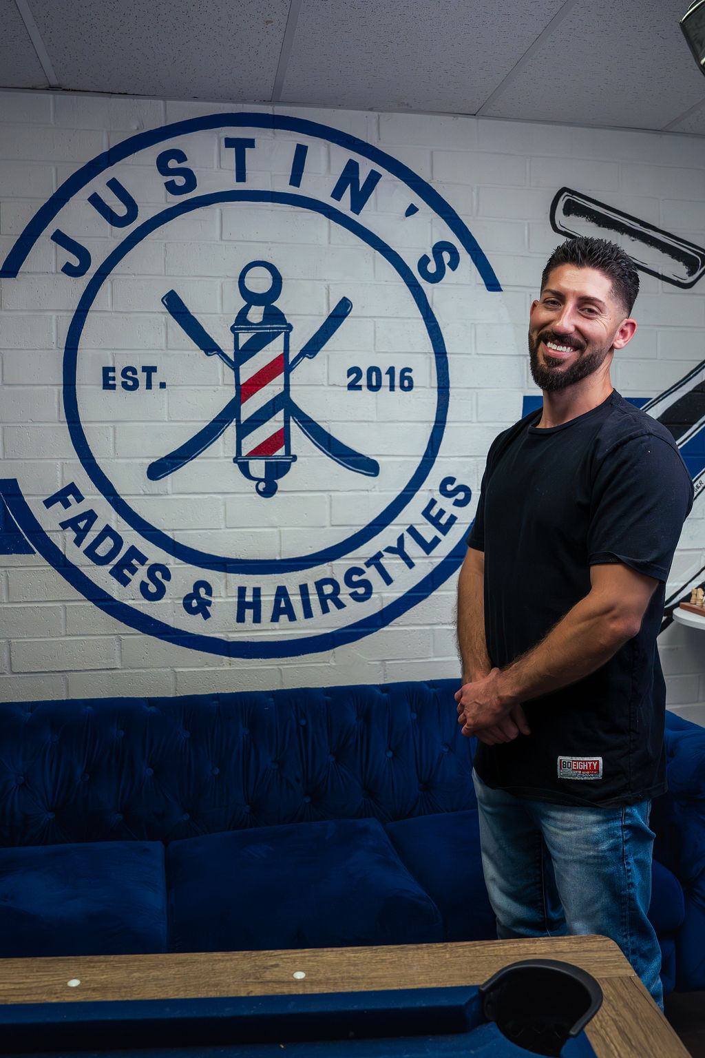 Justin Balint — owner of Justin's Fades & Hairstyles, standing by the shop's logo mural.